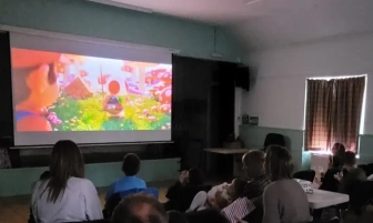 People watching an animated movie projected on a screen in a dimly lit room.